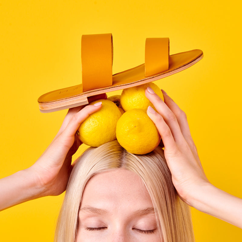 Maki Sandals in yellow colour placed on models head with three lemons.